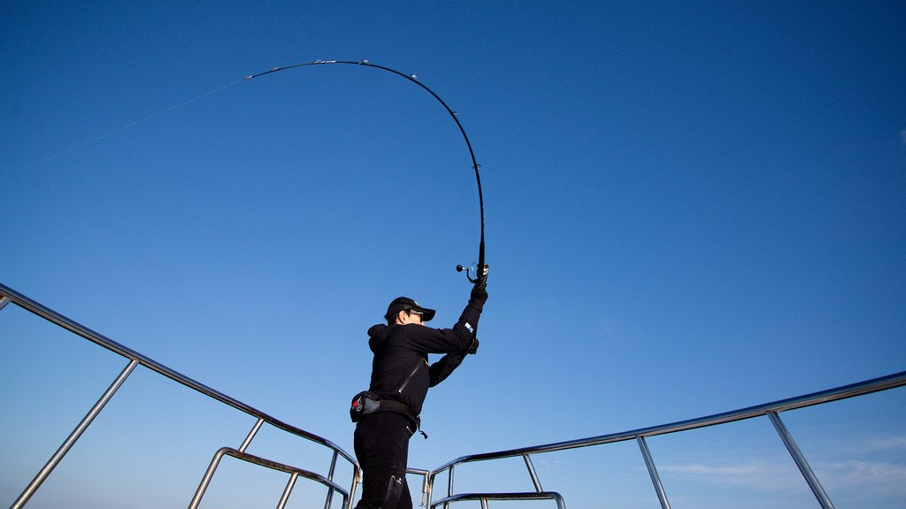 Angler on a boat with an offshore casting rod bent hard on a fish