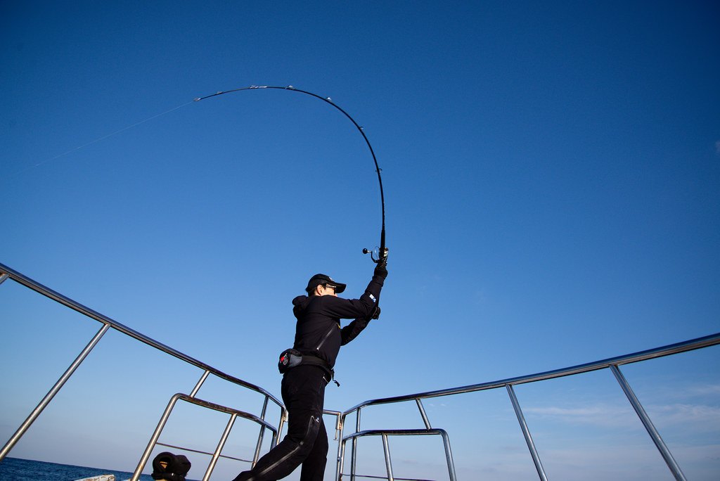 Angler on a boat with an offshore casting rod bent hard on a fish
