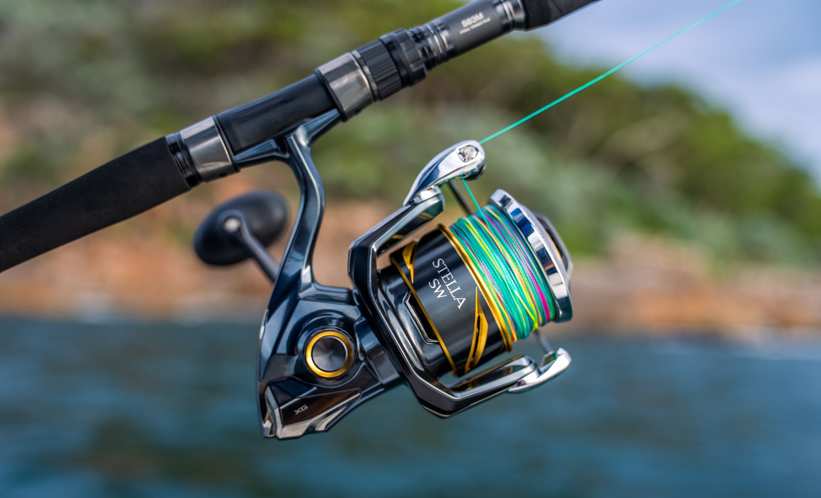 Close-up of a Shimano spinning reel spooled with braid on a fishing rod, with water behind
