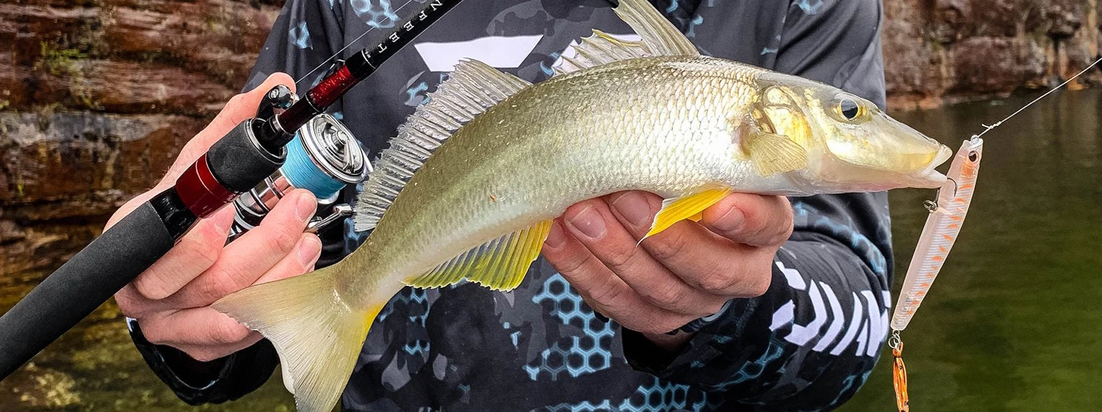 Angler holding a yellowfin whiting and a light spinning rod and reel, with a pink stickbait lure